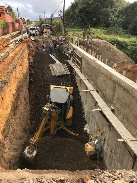 Retroexcavadora trabajando en una zanja junto a un muro de contención